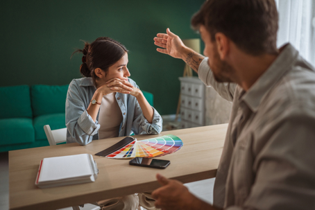oung couple having a serious debate and relationship conflict while choosing paint color swatches for their house renovation,